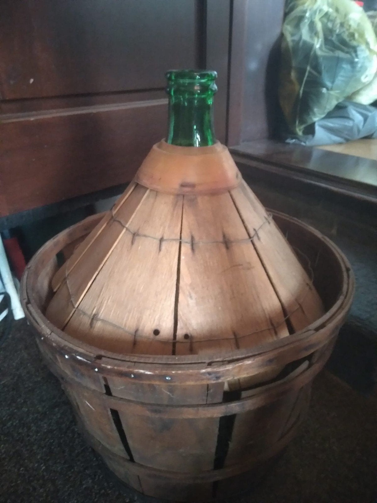 Grote groene glazen fles in houten mand, Ophalen