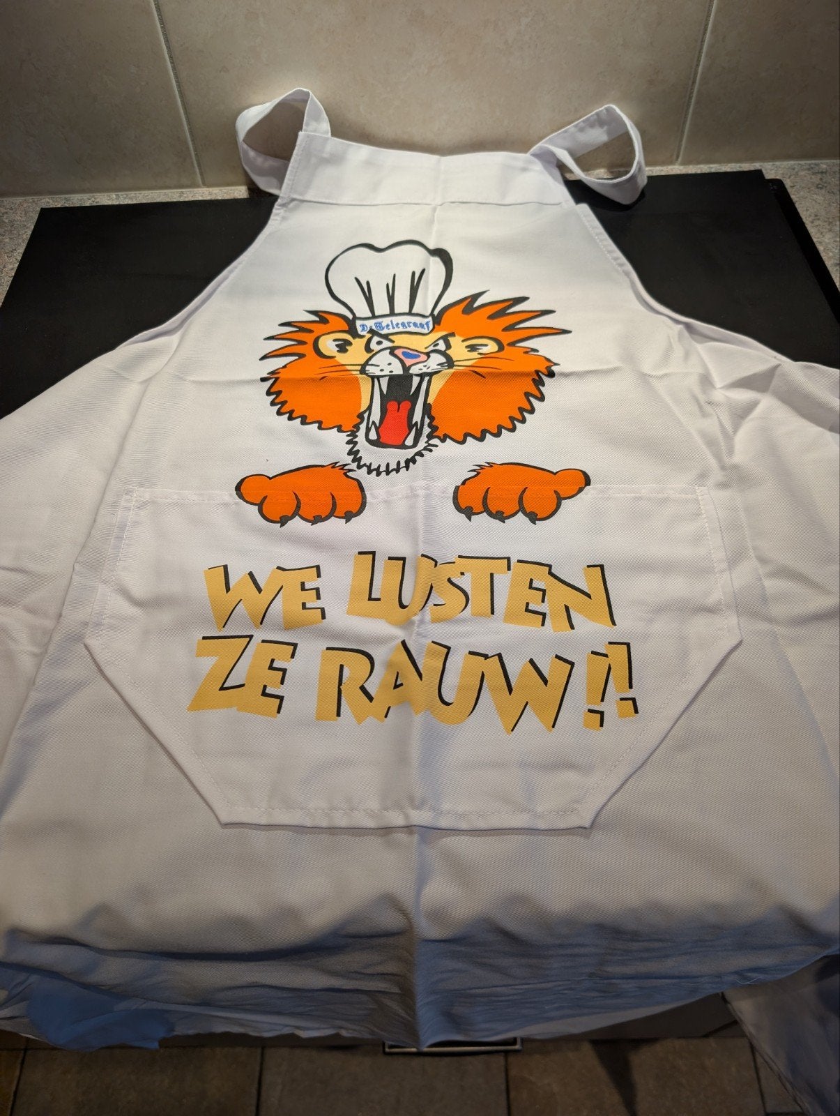 Grappig Telegraaf  Schort met Leeuw - "We lusten ze rauw!", Ophalen, Overige typen, Textiel, Zo goed als nieuw