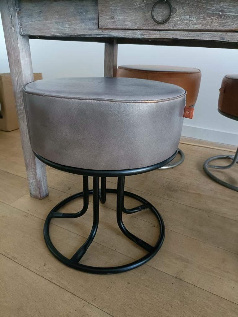 Grijze lederen poef met zwart metalen onderstel., Modern design, Rond, Ophalen of Verzenden, Zo goed als nieuw
