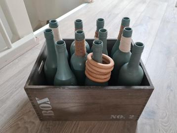 Krat met 11 flessen en 5 houten ringen (spel ringwerpen) beschikbaar voor biedingen