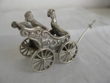 Zilveren miniatuur van een rijtuig met 2 personen.