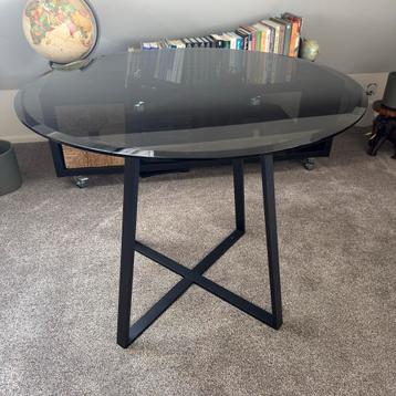 Stijlvolle ronde tafel met een donker getint glazen blad beschikbaar voor biedingen