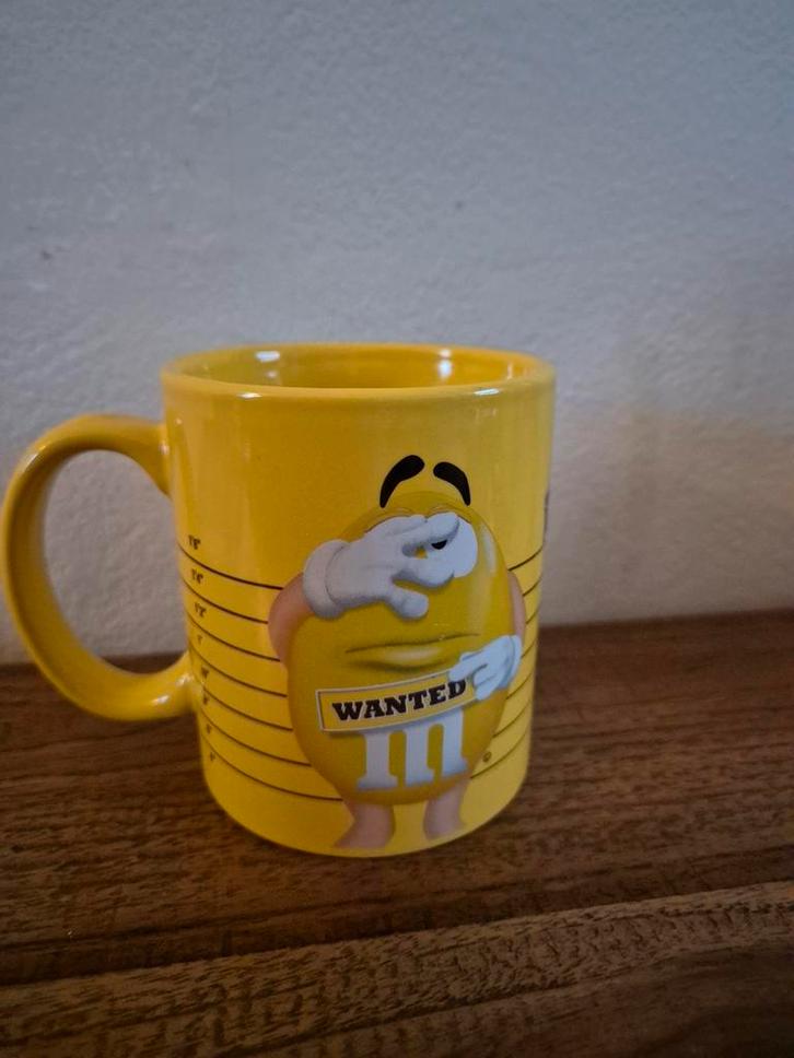Gele M&M's 'Wanted' mok ***zgan***, Huis en Inrichting, Keuken | Servies, Zo goed als nieuw, Kop(pen) en/of Schotel(s), Overige stijlen
