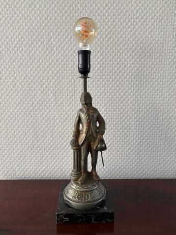 Antieke metalen lamp van een man staand naast een zuil. beschikbaar voor biedingen