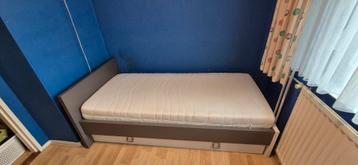 1 persoons bed met matras en lade op wieltjes eronder.