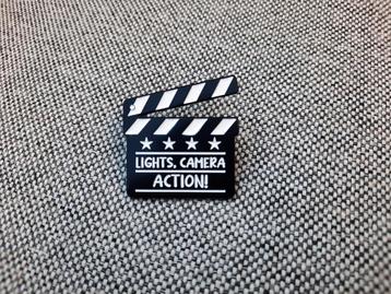 1 pin van een filmklapper met de tekst Lights, Camera ACTION beschikbaar voor biedingen